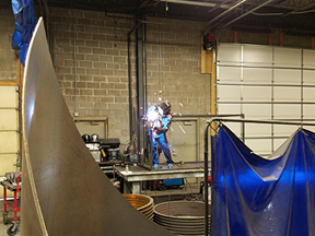 Welder welding a metal frame with tank and other items in foreground